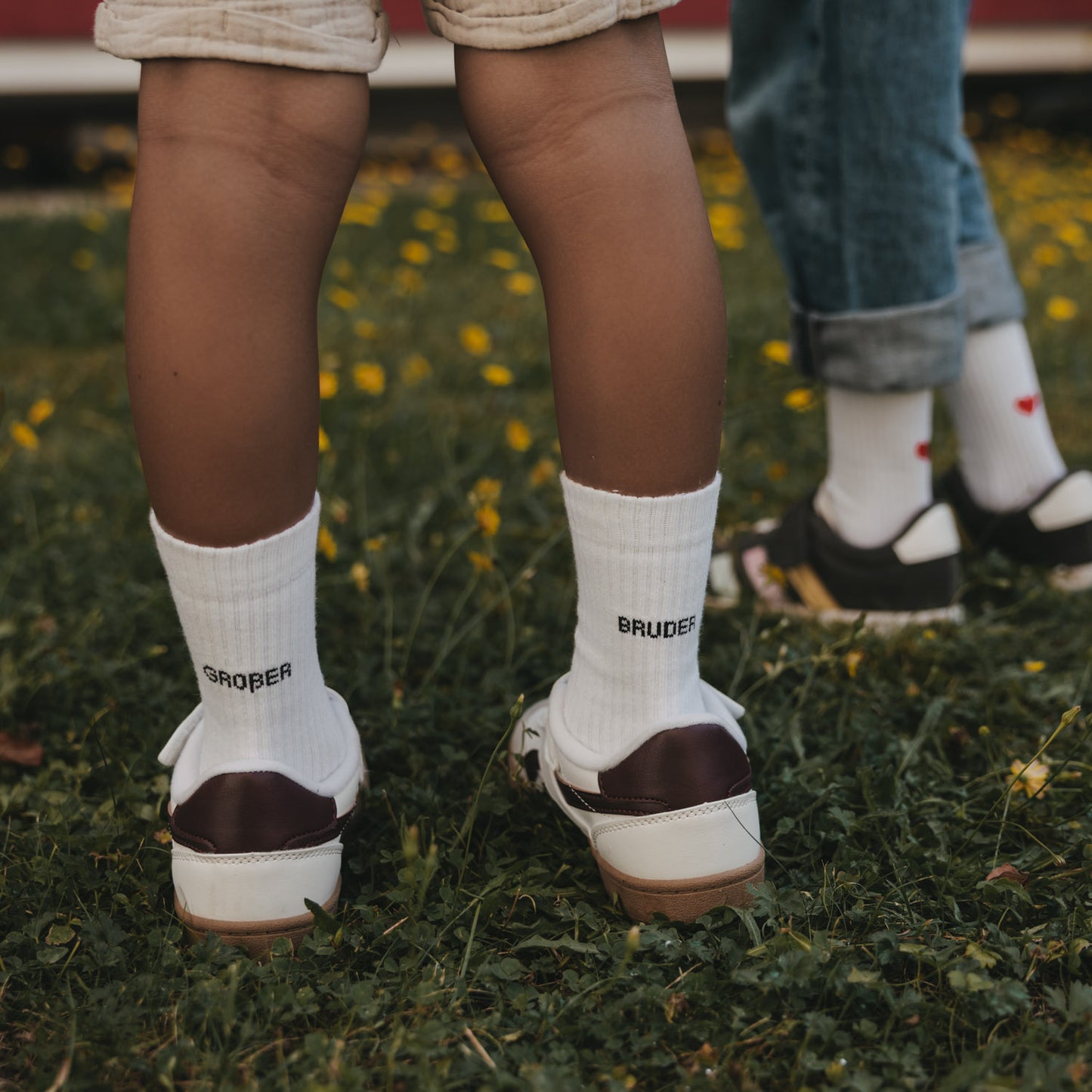 Kids Socken Großer Bruder in Weiß mit schwarzem Schriftzug zu Sneakern auf einer Wiese