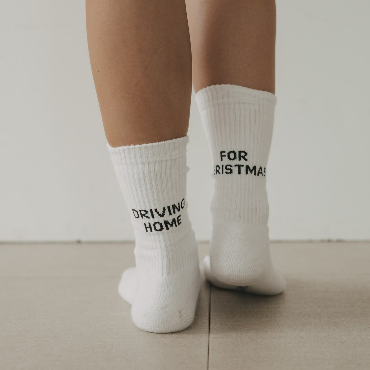 Weiße Socken Driving Home for Christmas mit schwarzem Schriftzug von hinten getragen