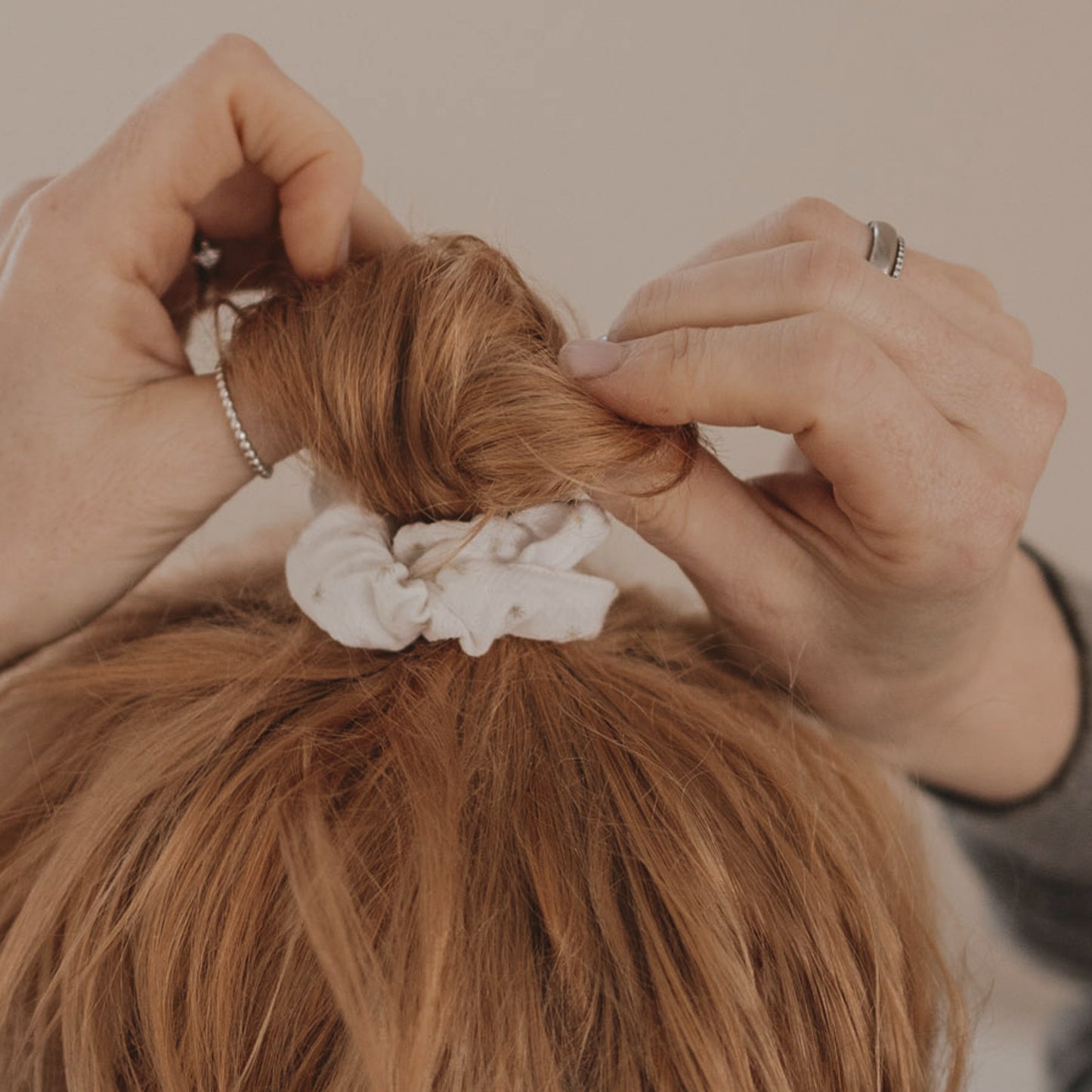 Hände stylen Dutt mit weißem Scrunchie mit Blumenmuster