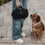 Hund blickt zu schwarzer Hundedecke in Hand einer Person auf Gehweg