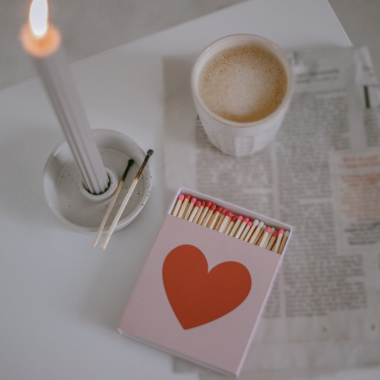 Offene Streichholzschachtel mit Herzdesign neben Kerze und Kaffee auf einem Tisch.