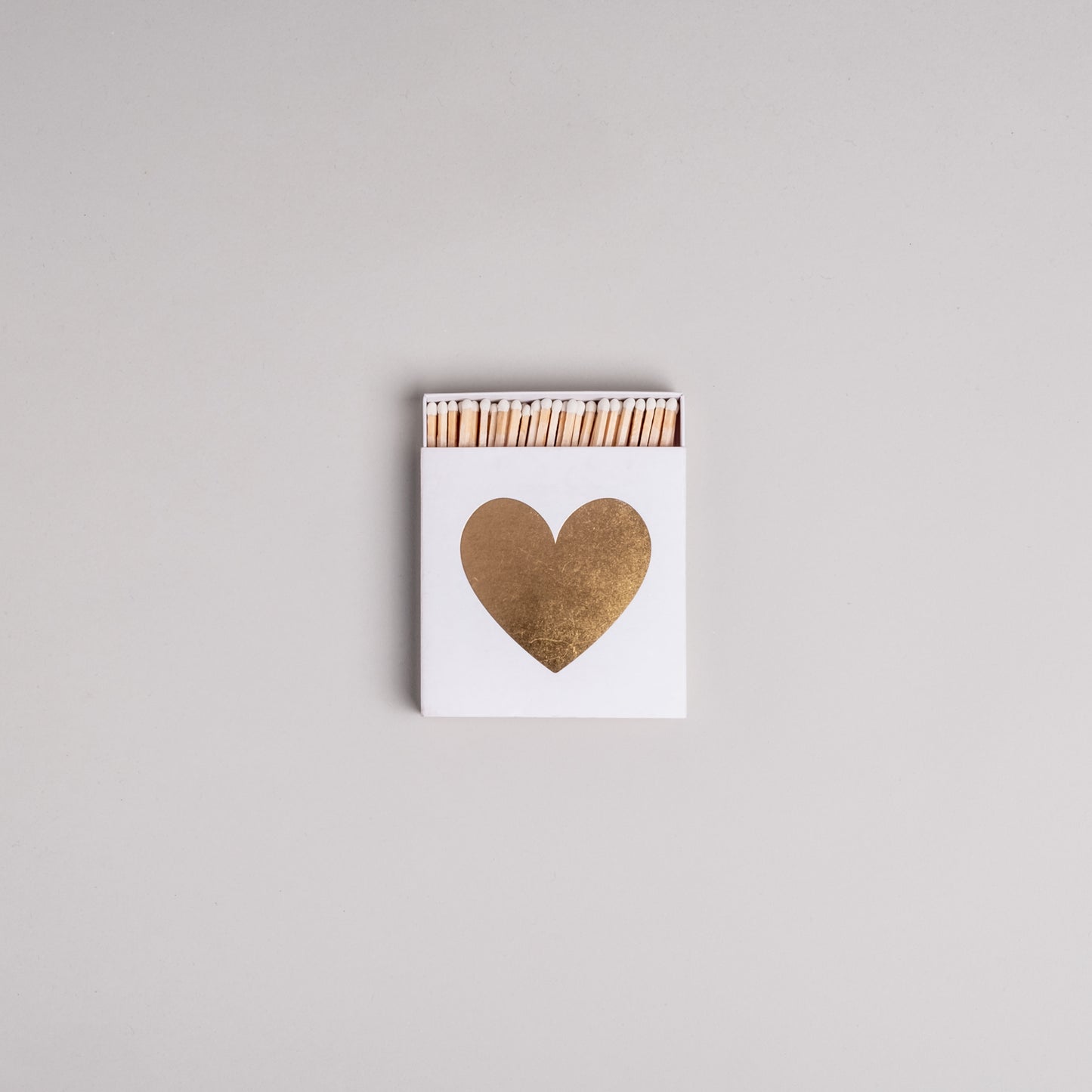 Weiße Streichholzschachtel mit goldenem Herz auf hellem Hintergrund – dekorativ und stilvoll.