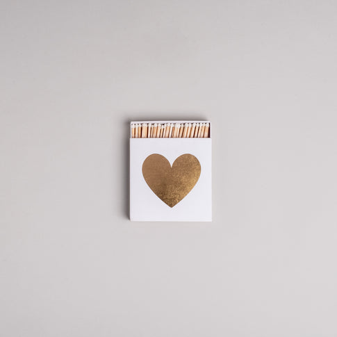 Weiße Streichholzschachtel mit goldenem Herz auf hellem Hintergrund – dekorativ und stilvoll.