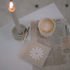 Streichhölzer Daisy neben Kerze und Kaffee auf Zeitung – gemütliche Morgenstimmung mit stilvollem Zubehör.