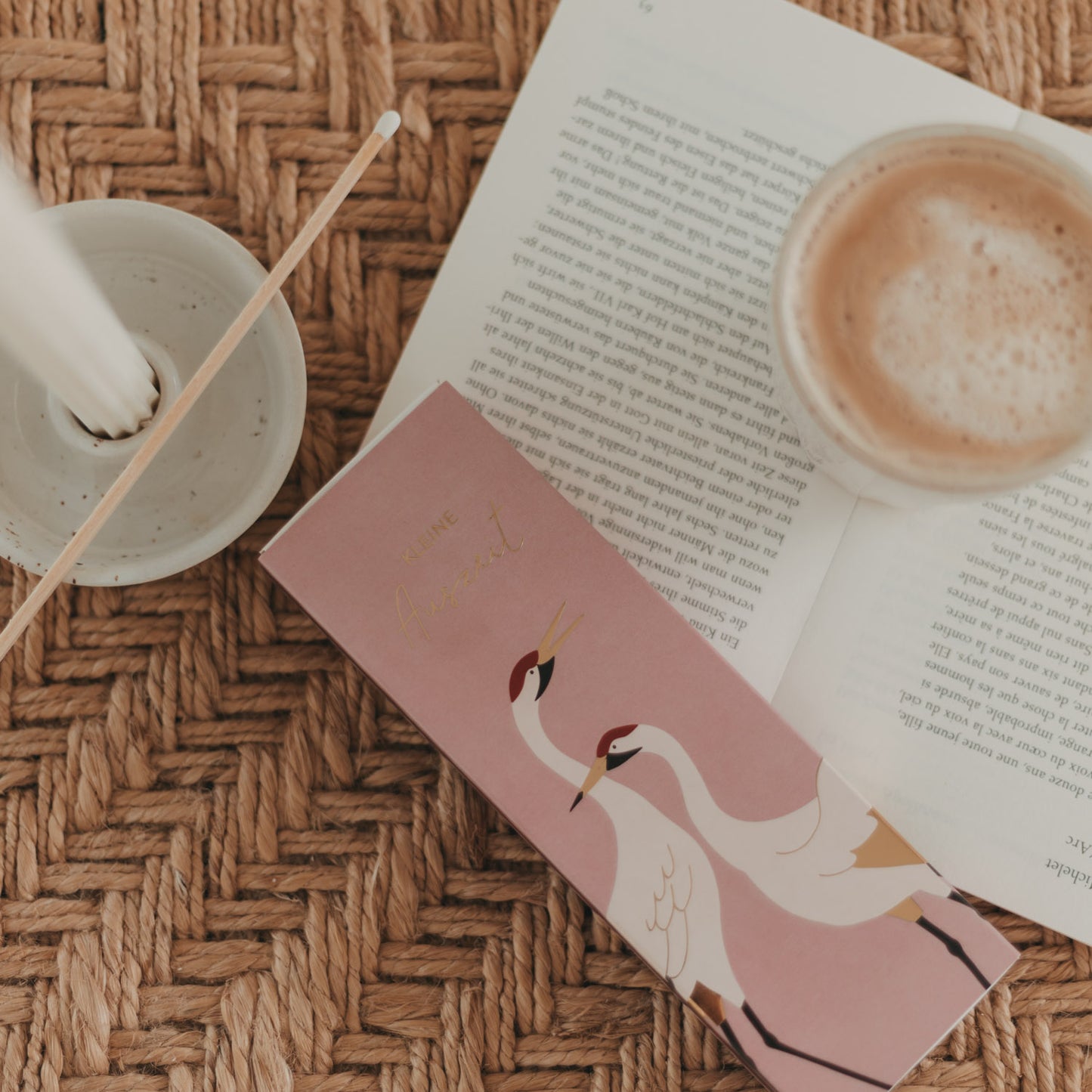 Streichholzschachtel „Kleine Auszeit“ mit Kranichen neben Buch und Kaffeetasse