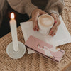 Streichholzschachtel „Kleine Auszeit“ mit Kranich-Motiv neben Kerze und Kaffeetasse