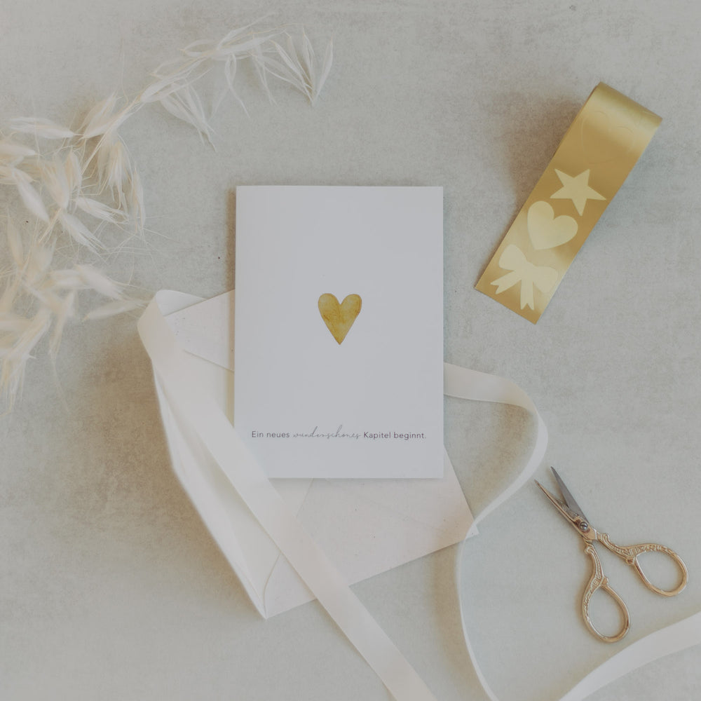 Grußkarte mit goldenem Herz, Stickerrolle Stern-Herz-Schleife Gold und Schere auf hellem Untergrund
