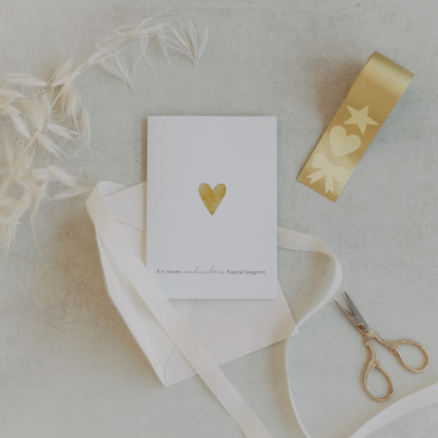 Grußkarte mit goldenem Herz, Stickerrolle Stern-Herz-Schleife Gold und Schere auf hellem Untergrund