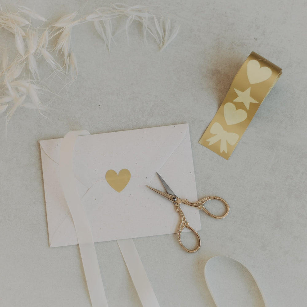 Stickerrolle mit goldenen Motiven Herz, Stern, Schleife und Schere auf hellem Untergrund