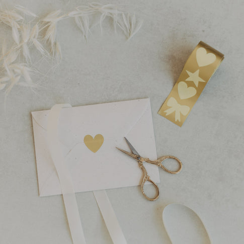 Stickerrolle mit goldenen Motiven Herz, Stern, Schleife und Schere auf hellem Untergrund