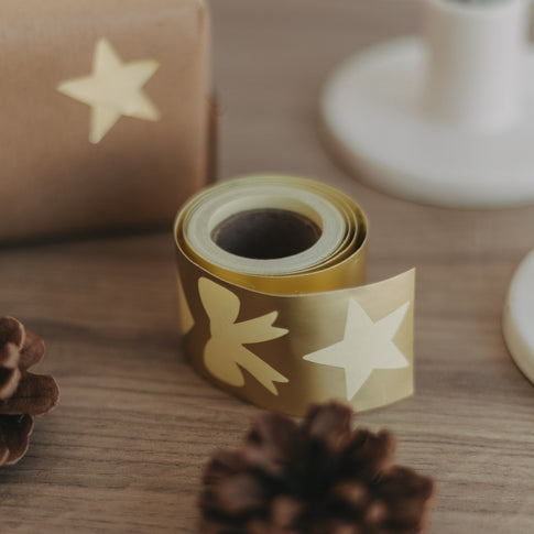 Goldene Stickerrolle mit Motivansicht auf Holzuntergrund, daneben verpacktes Geschenk