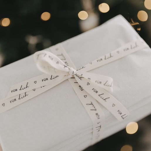 Geschenk mit beigefarbenem Baumwollband „Für dich“, dekorativ verpackt vor warmen Lichtern.