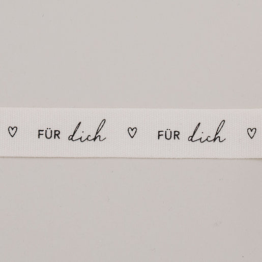 Detailaufnahme vom Geschenkband „Für dich“ mit Herzen, schwarzer Schrift auf weißem Baumwollband.