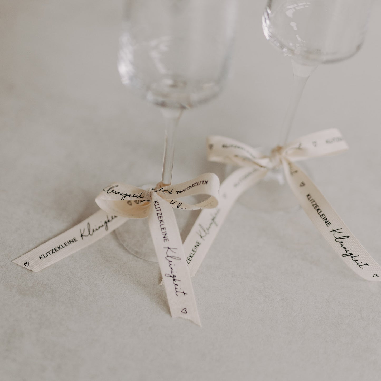 Detailansicht von Sektgläsern mit gebundenem Geschenkband „Klitzekleine Kleinigkeit“.