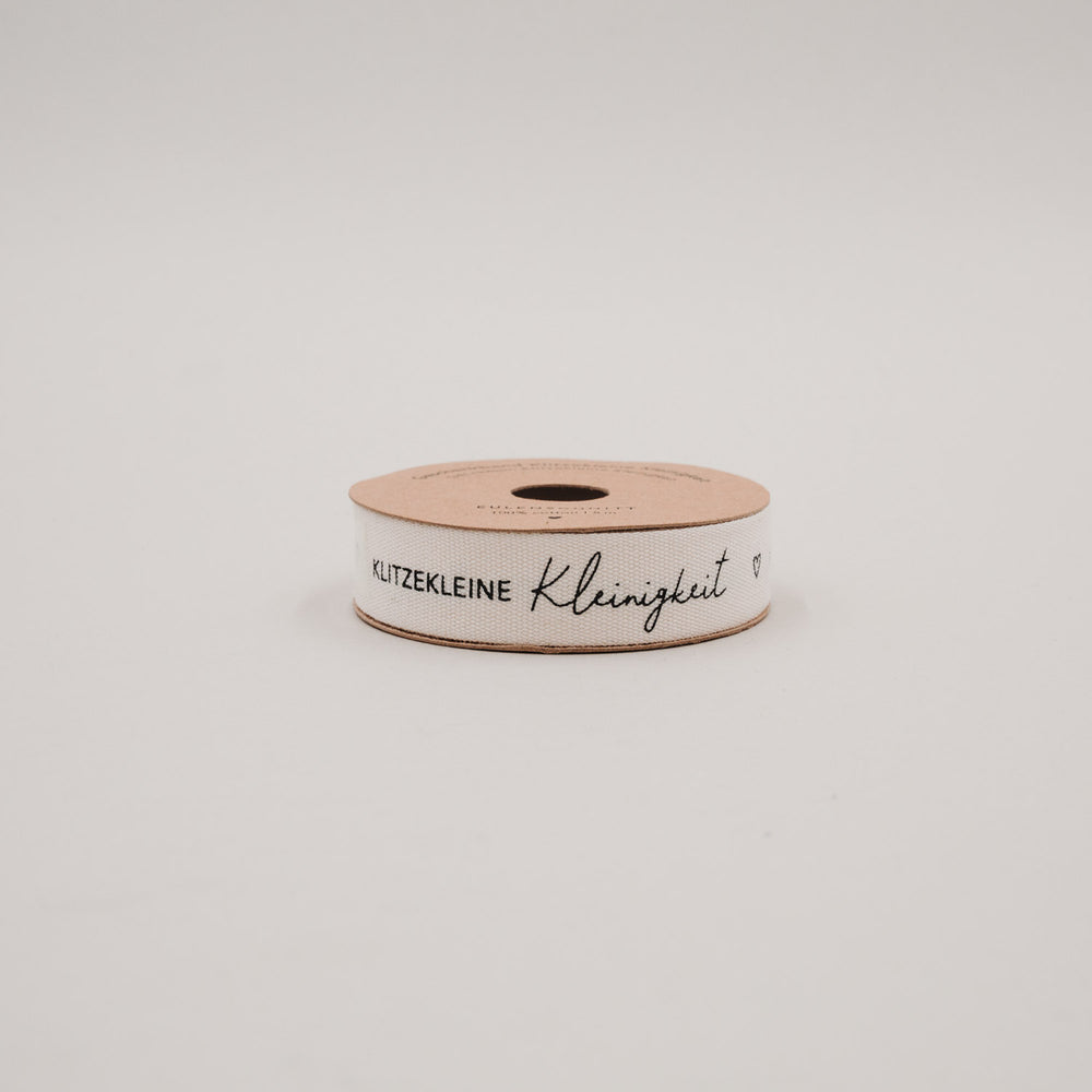 Seitliche Ansicht der Geschenkbandrolle „Klitzekleine Kleinigkeit“ mit schwarzem Schriftzug auf Naturband