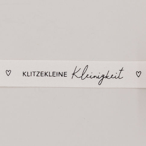 Nahaufnahme des Baumwollbands mit Aufdruck „Klitzekleine Kleinigkeit“ und kleinen Herzsymbolen