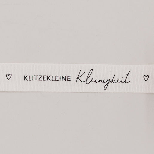 Nahaufnahme des Baumwollbands mit Aufdruck „Klitzekleine Kleinigkeit“ und kleinen Herzsymbolen
