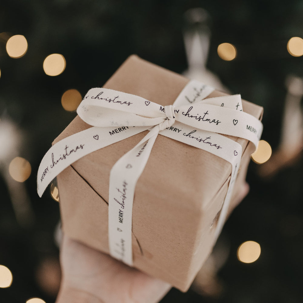 Geschenk mit Baumwollband Merry Christmas liebevoll verpackt vor Weihnachtsbaumlichtern