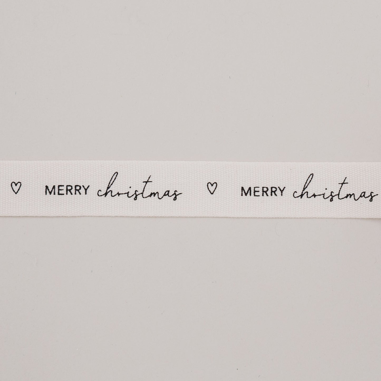 Detailaufnahme Geschenkband Merry Christmas mit Herzmotiv auf naturweißem Baumwollband