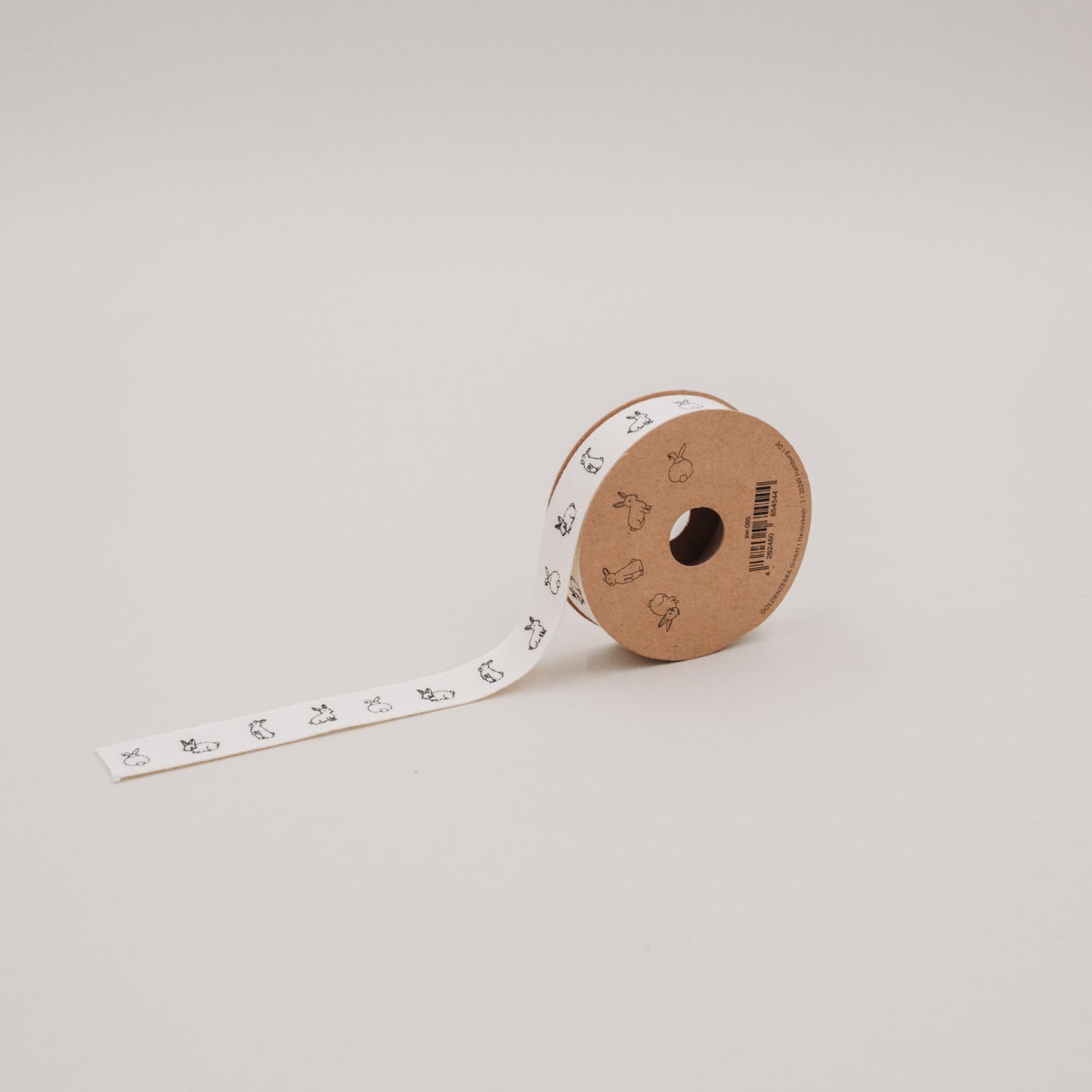 Rolle Geschenkband mit Kaninchenmotiv auf Kartonspule, ausgerollt auf hellem Hintergrund.