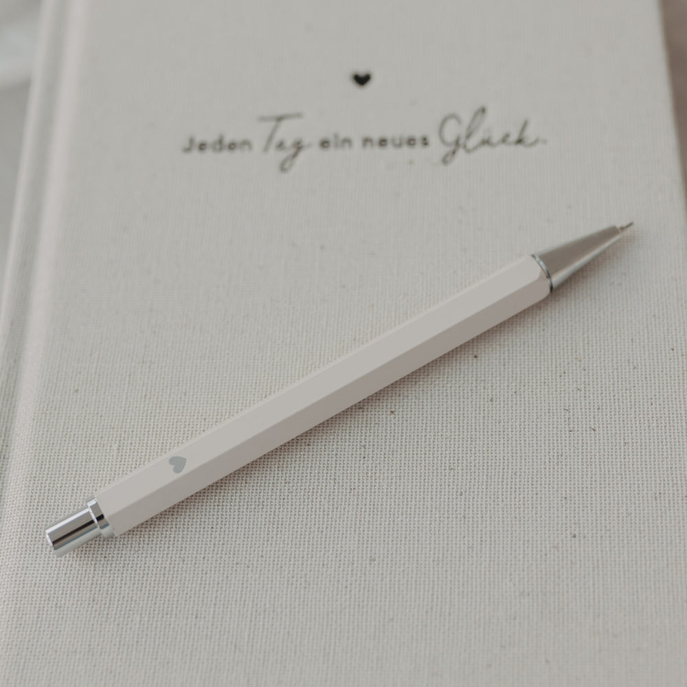 Druckbleistift Creme auf Notizbuch mit feiner Struktur und Herzmotiv.