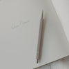 Grauer Druckbleistift auf offener Notizbuchseite mit Schriftzug ‚Dein Name‘.