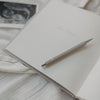 Grauer Druckbleistift auf offenem Notizbuch, umgeben von sanften Stoffen und Ultraschallbild.