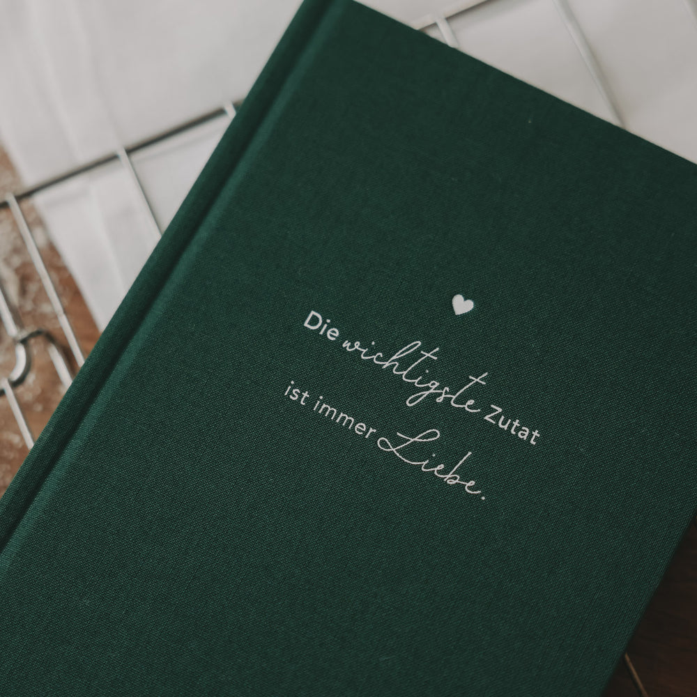 Detailaufnahme des grünen Rezeptbuchs mit geprägtem Spruch „Die wichtigste Zutat ist immer Liebe“.