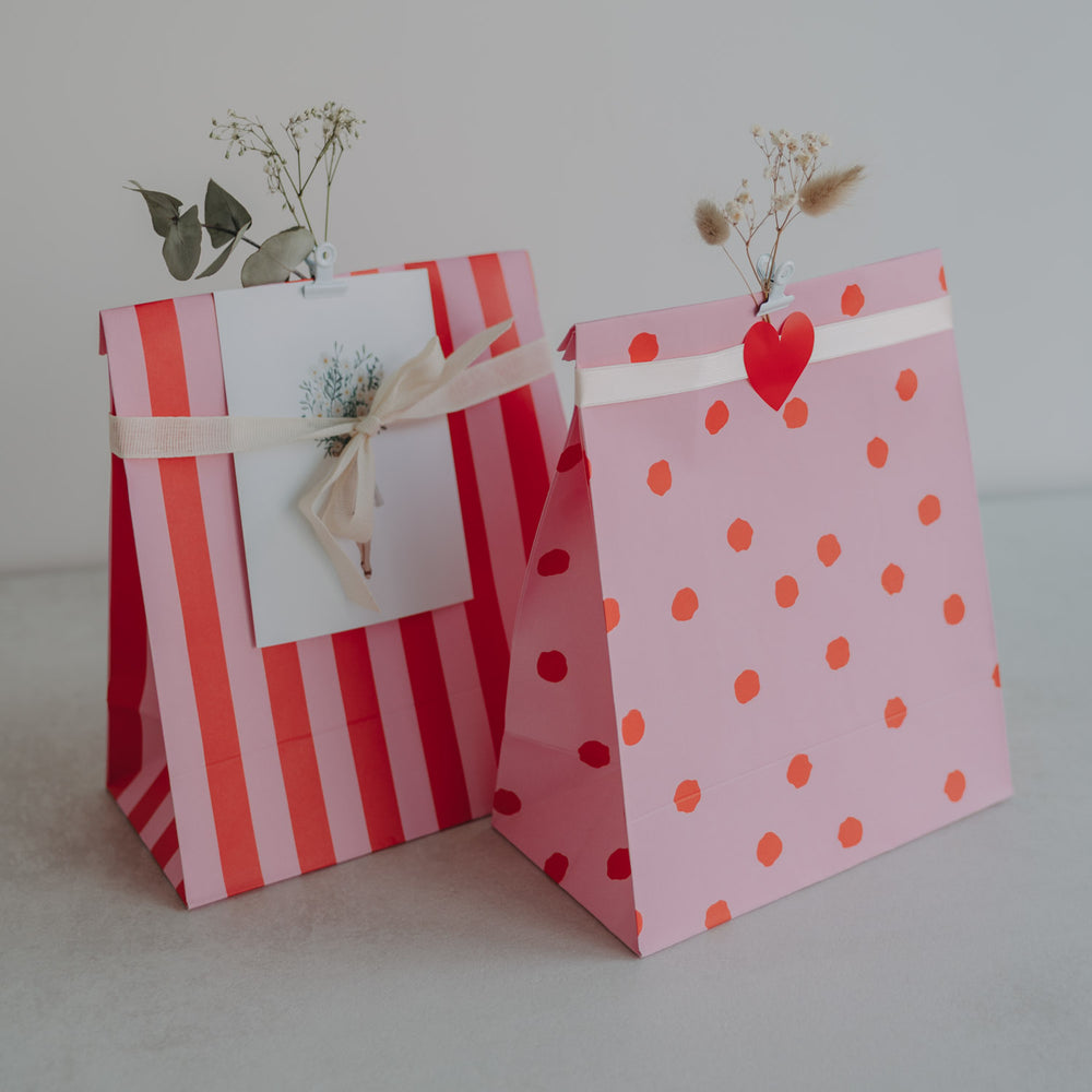 Bunte Geschenktüten aus Papier in Rot und Rosa mit Punkten, dekoriert mit Herz und Trockenblumen.