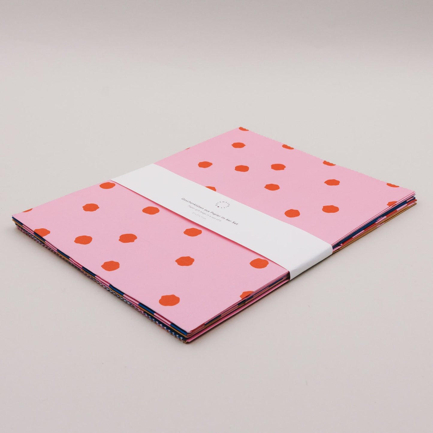 Papier-Geschenktüten im 6er Set, flach gefaltet, buntes Streifen- und Punktdesign.