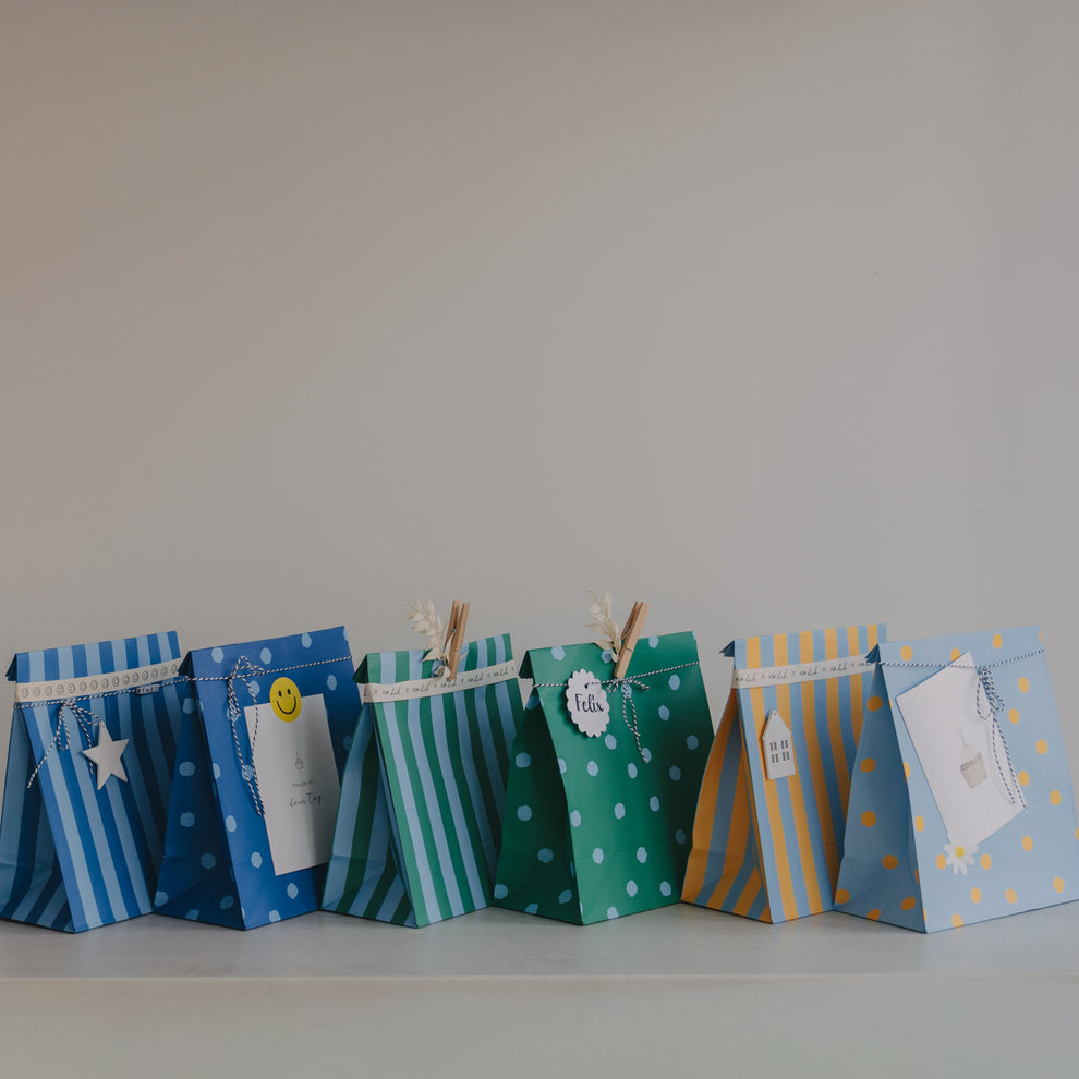 Geschenktüten aus Papier in Blau, Grün und Gelb mit Punkten und Streifen, dekorativ aufgereiht