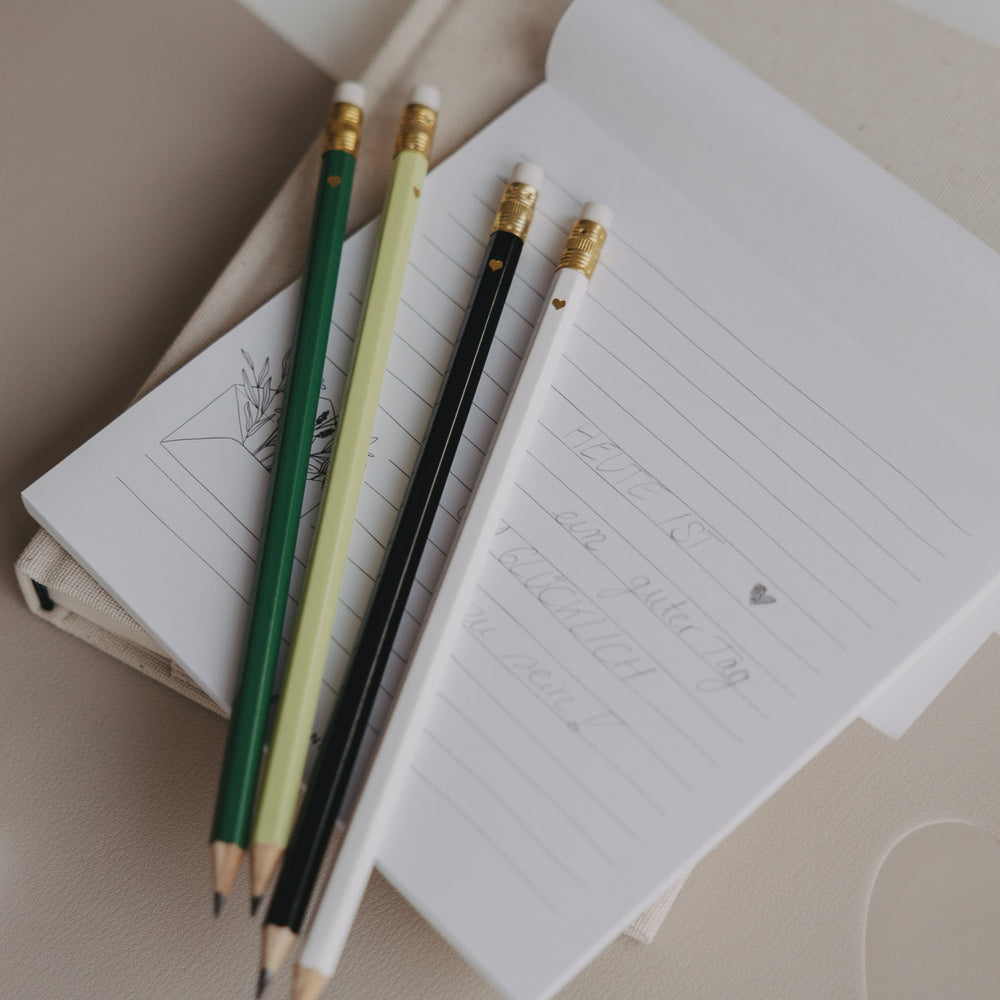 Vier Bleistifte in Grün, Weiß, Schwarz und Hellgrün auf Notizblock