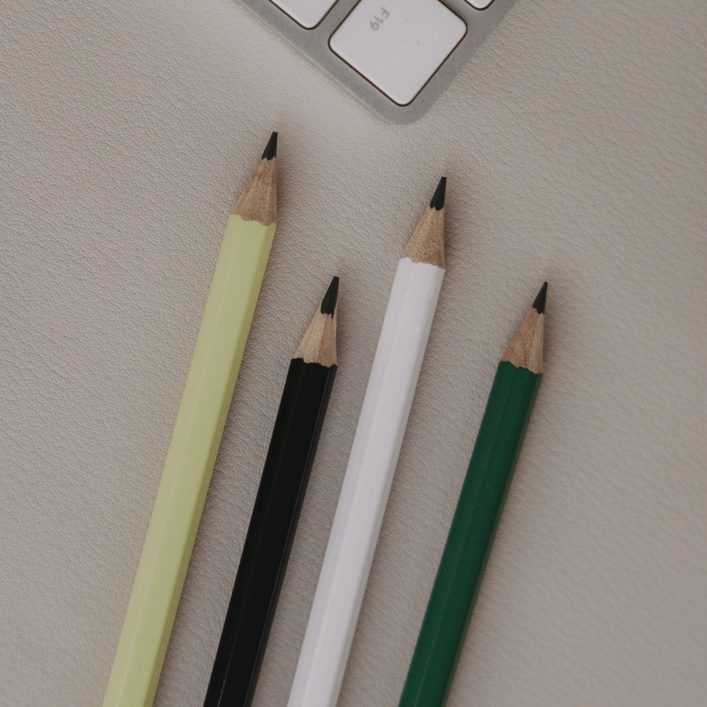 Vier angespitzte Bleistifte in Grün, Weiß, Schwarz und Hellgrün auf Schreibtisch