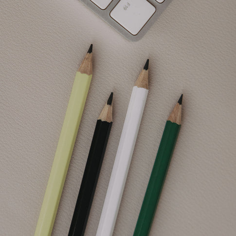 Vier angespitzte Bleistifte in Grün, Weiß, Schwarz und Hellgrün auf Schreibtisch