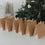 Weihnachtliche Geschenktüten aus Kraftpapier mit Holzklammern vor geschmücktem Weihnachtsbaum