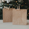 Geschenktüte aus Kraftpapier mit weißer Häuserillustration und Schriftzug „Für dich“ vor Weihnachtsbaum