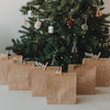 Weihnachtliche Kraftpapier-Geschenktüten mit verschiedenen weißen Motiven vor beleuchtetem Tannenbaum