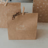 Braune Geschenktüte aus Kraftpapier mit weißem Schriftzug „Frohe Weihnachten“ und Holzklammer