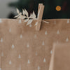 Braune Geschenktüte mit weißen Weihnachtsbaum-Motiven, Holzklammer und dekorativem Zweig