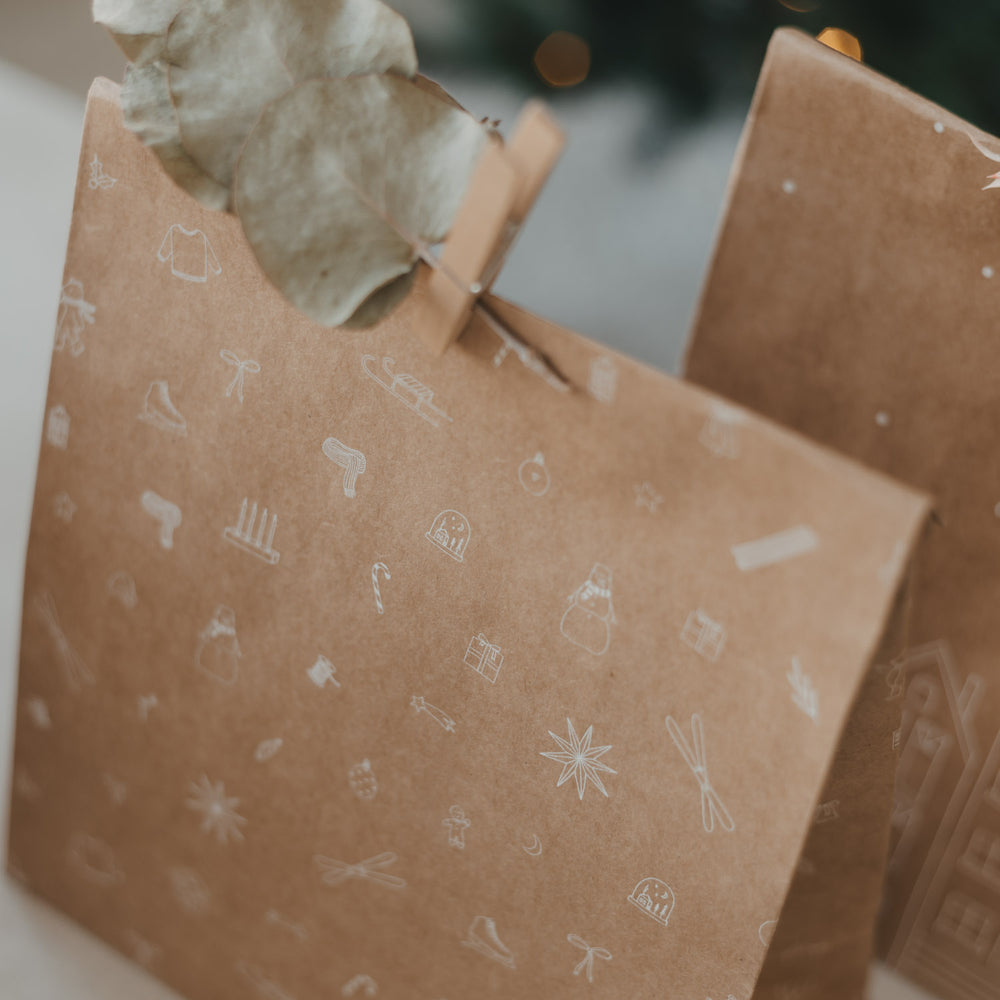 Braune Geschenktüte mit feinen weißen Weihnachtsmotiven, Eukalyptus und Holzklammer