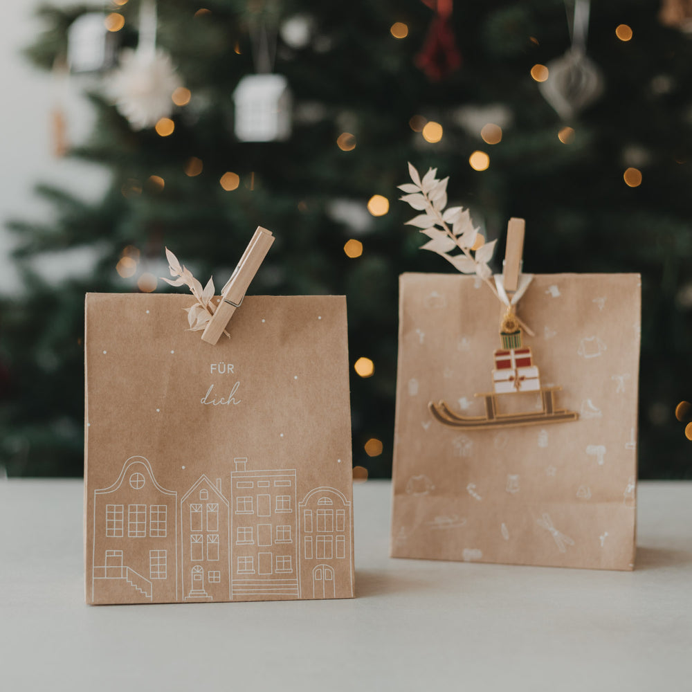 Geschenktüte aus Kraftpapier mit „Für dich“ und Häuser-Motiv neben weihnachtlich dekorierter Tüte