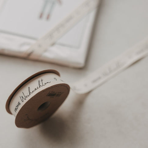 Eulenschnitt Geschenkband Frohe Weihnachten auf Rolle neben weihnachtlich verpacktem Geschenk
