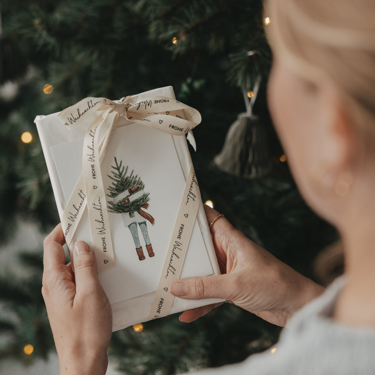 Weihnachtsgeschenk mit Eulenschnitt Geschenkband Frohe Weihnachten in den Händen vor dem Weihnachtsbaum